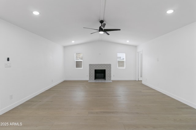 unfurnished living room with ceiling fan, a fireplace, vaulted ceiling, and light wood-type flooring