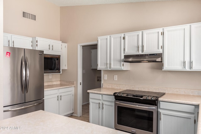 kitchen with a textured ceiling, light tile patterned floors, stainless steel appliances, and white cabinets