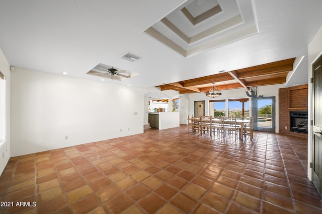 unfurnished living room featuring beam ceiling, a brick fireplace, ceiling fan with notable chandelier, and dark tile patterned floors