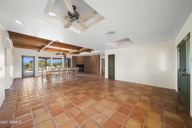 unfurnished living room with ceiling fan with notable chandelier, a fireplace, tile patterned flooring, a tray ceiling, and beam ceiling