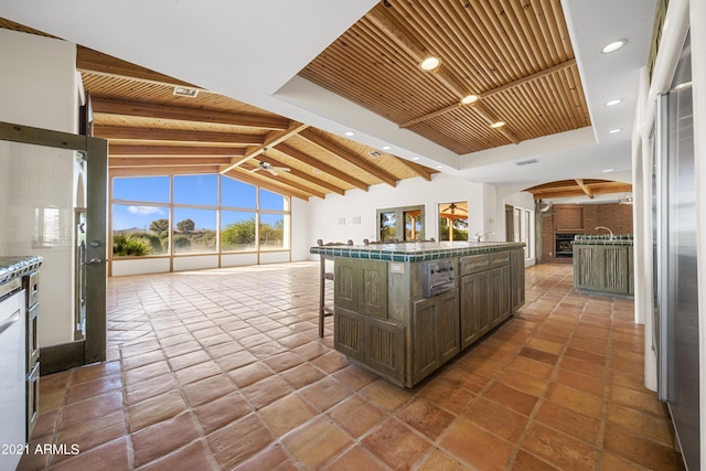 kitchen featuring wood ceiling, stainless steel refrigerator, vaulted ceiling with beams, a kitchen breakfast bar, and a fireplace