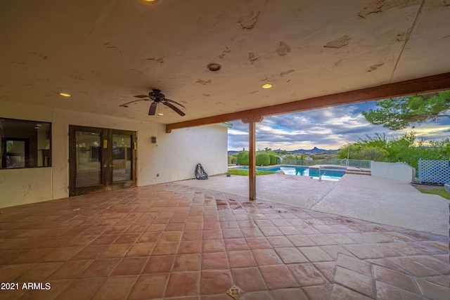 patio terrace at dusk featuring a fenced in pool, ceiling fan, and french doors