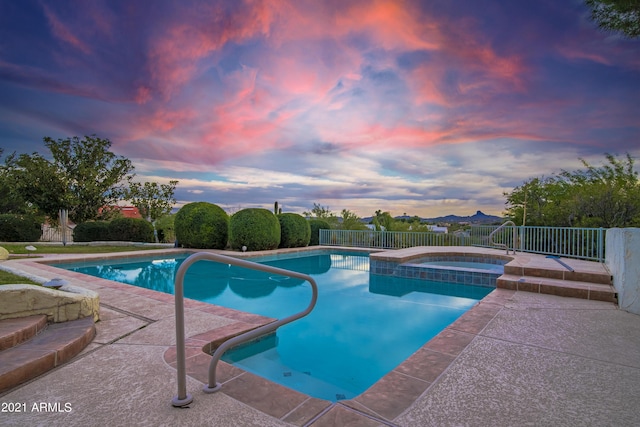 pool at dusk with a patio area and an in ground hot tub