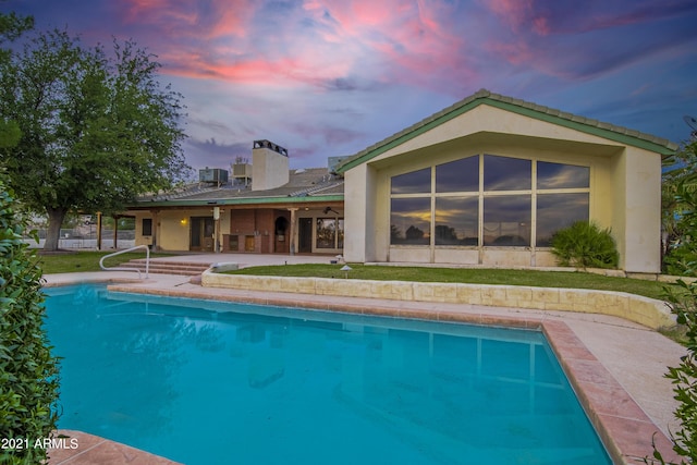 pool at dusk with a patio and central air condition unit