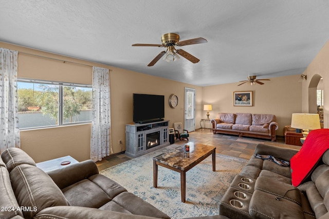 living room with ceiling fan, a textured ceiling, and a fireplace