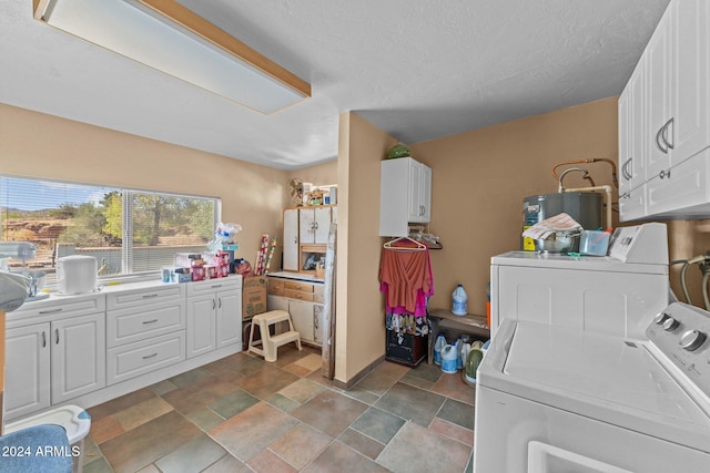 laundry room with cabinets, water heater, a textured ceiling, and washer and clothes dryer