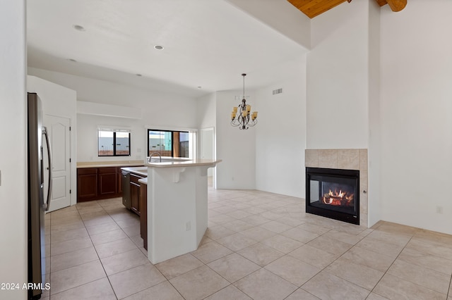 kitchen featuring light tile patterned flooring, a tile fireplace, stainless steel refrigerator, a kitchen island, and hanging light fixtures