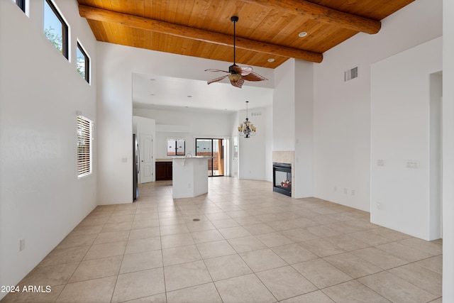 unfurnished living room with wood ceiling, ceiling fan with notable chandelier, a towering ceiling, light tile patterned floors, and a fireplace