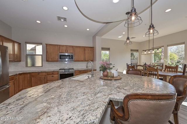 kitchen featuring a breakfast bar, stainless steel appliances, visible vents, a sink, and light stone countertops