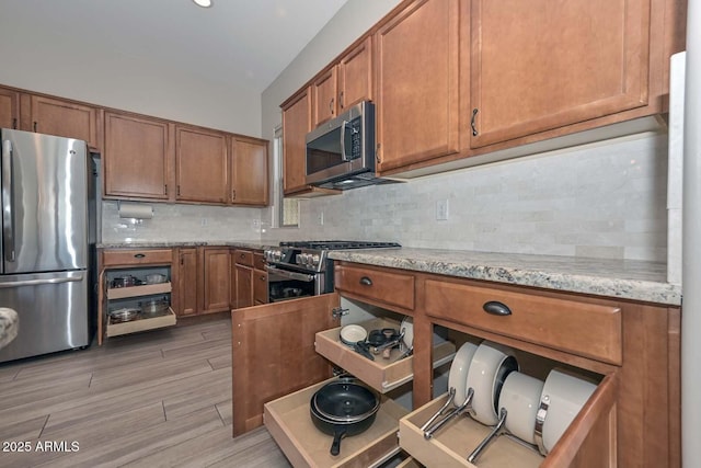 kitchen with brown cabinets, light stone counters, stainless steel appliances, and backsplash