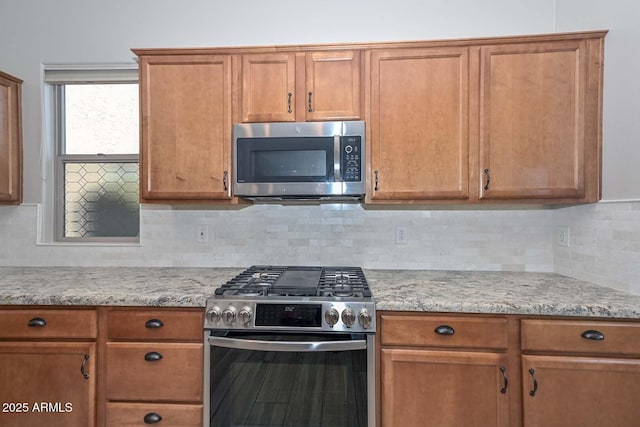 kitchen featuring stainless steel appliances, brown cabinets, backsplash, and light stone countertops