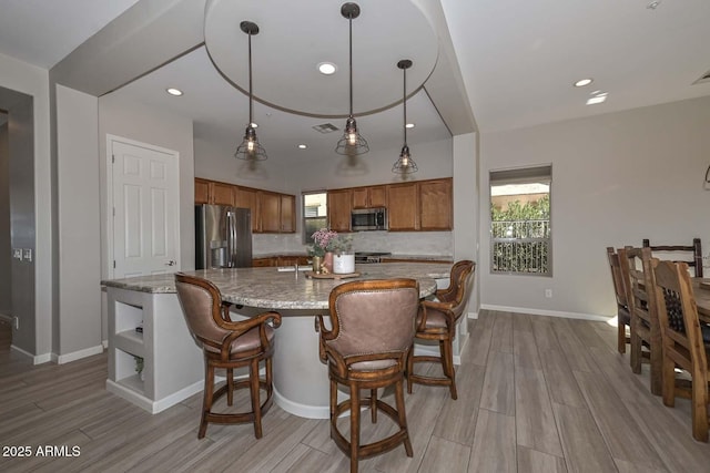 kitchen with light stone counters, pendant lighting, visible vents, appliances with stainless steel finishes, and brown cabinetry