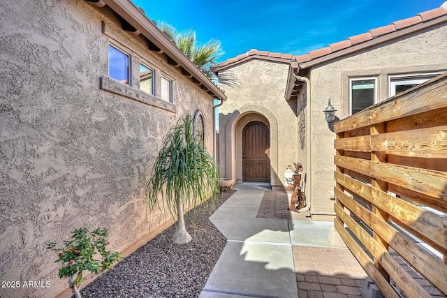 property entrance featuring fence, a patio, a tiled roof, and stucco siding