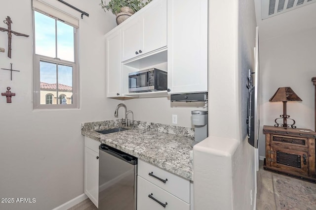 kitchen with appliances with stainless steel finishes, a sink, light stone countertops, and white cabinets