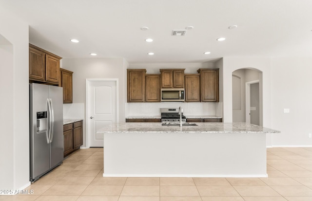 26949 W Lone Cactus Dr, Buckeye, AZ 85396 - kitchen with appliances with stainless steel finishes, recessed lighting, arched walkways, an island with sink, and light stone countertops