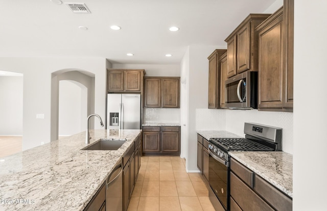 26949 W Lone Cactus Dr, Buckeye, AZ 85396 - kitchen featuring appliances with stainless steel finishes, a sink, arched walkways, light stone countertops, and recessed lighting