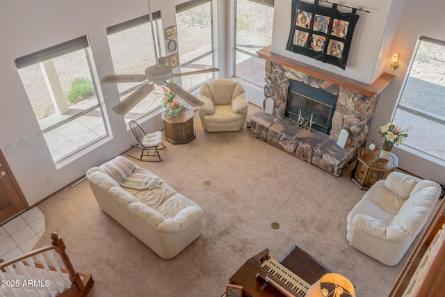 carpeted living area featuring ceiling fan and a stone fireplace