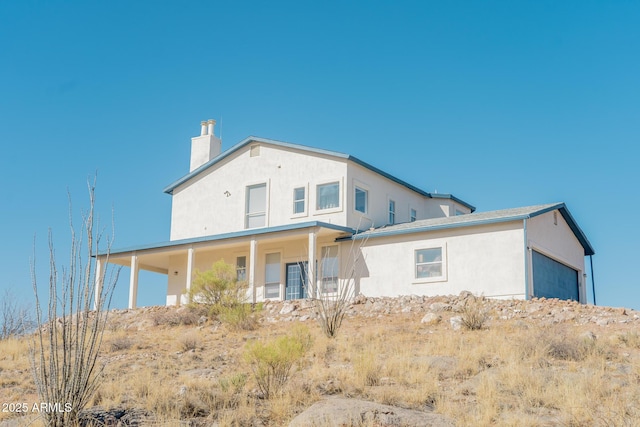 rear view of house with a chimney and stucco siding