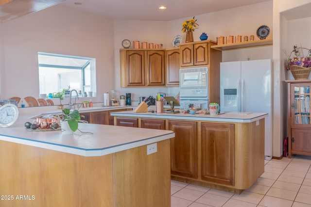 kitchen featuring brown cabinets, light tile patterned floors, light countertops, white appliances, and a peninsula