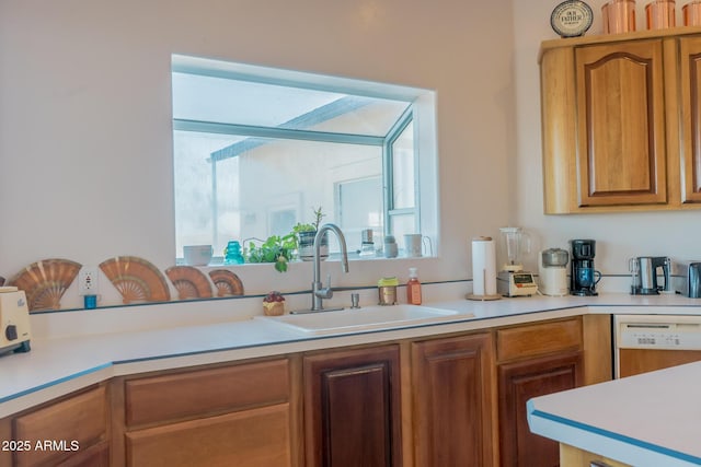 kitchen featuring light countertops, white dishwasher, a sink, and brown cabinets