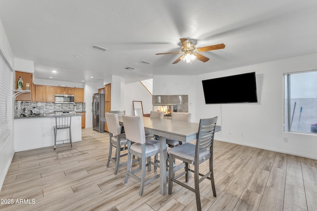 dining room with ceiling fan, a fireplace, and light hardwood / wood-style flooring