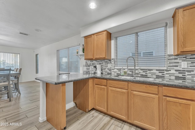 kitchen featuring tasteful backsplash, sink, kitchen peninsula, and dark stone countertops