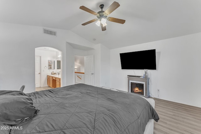 bedroom with lofted ceiling, light wood-type flooring, connected bathroom, and ceiling fan