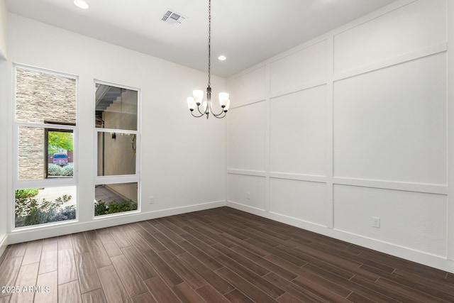 empty room with dark wood-style flooring, visible vents, a chandelier, and a decorative wall