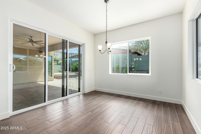 spare room with baseboards, wood finished floors, and ceiling fan with notable chandelier