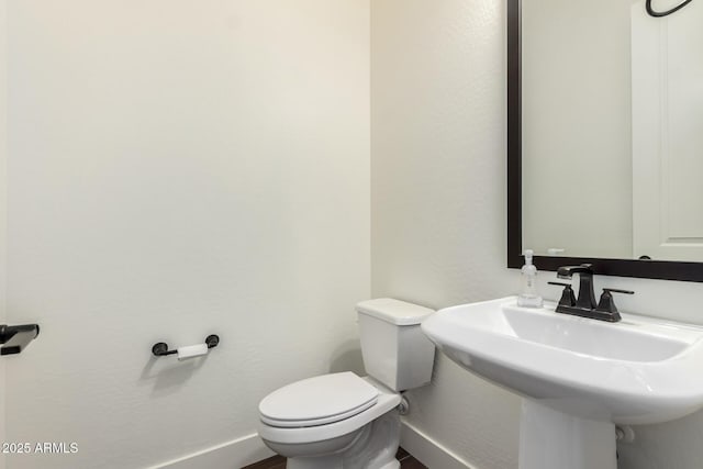 half bath featuring baseboards, a sink, and toilet