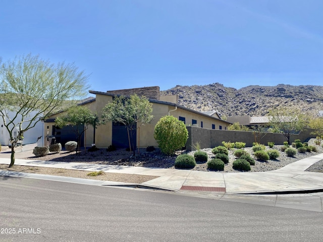 view of front of home with a mountain view, stucco siding, fence, and an attached garage