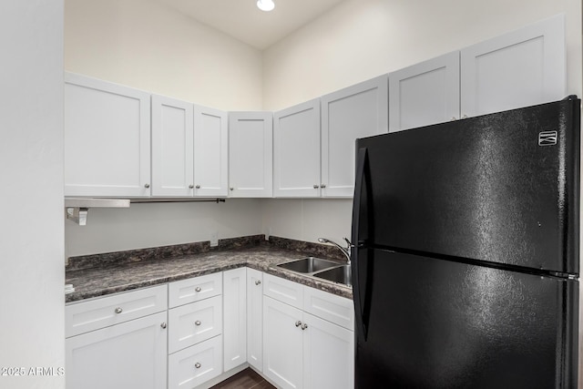 kitchen featuring white cabinets, dark wood-style floors, dark countertops, a sink, and freestanding refrigerator