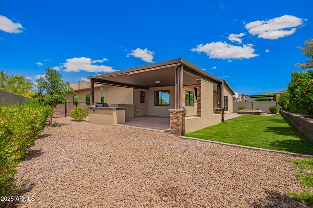 rear view of property featuring an outdoor kitchen, a fenced backyard, a yard, stucco siding, and a patio