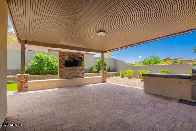 view of patio with exterior kitchen, an outdoor stone fireplace, and a fenced backyard