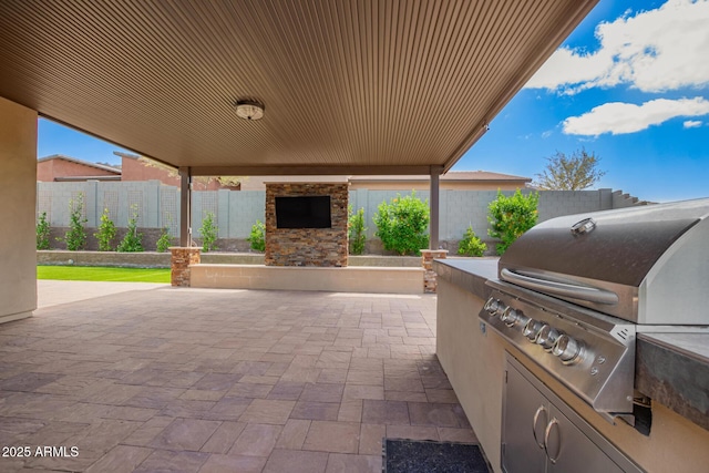 view of patio / terrace featuring area for grilling, an outdoor stone fireplace, an outdoor kitchen, and a fenced backyard