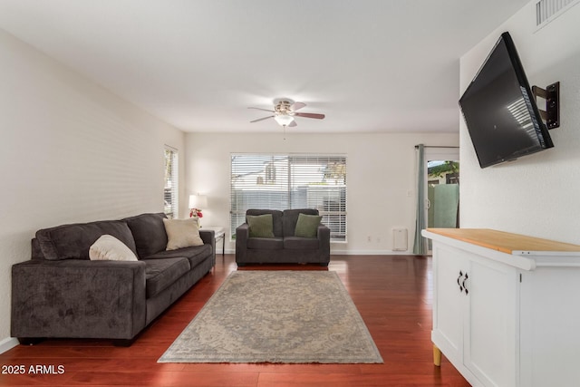 living room with dark wood-style floors, visible vents, baseboards, and a ceiling fan