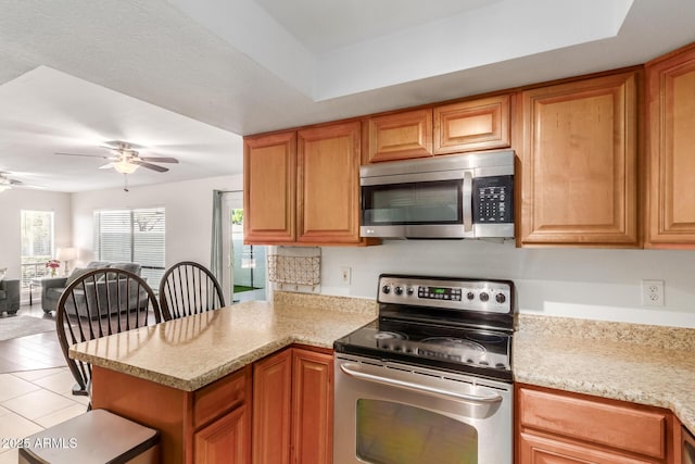 kitchen with stainless steel appliances, brown cabinetry, a ceiling fan, open floor plan, and a peninsula