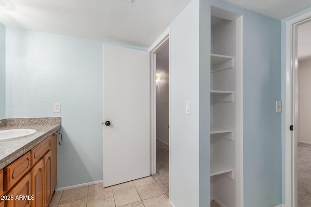 bathroom with a textured ceiling, built in shelves, vanity, baseboards, and tile patterned floors