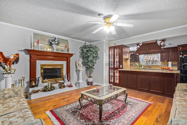 living room with a tile fireplace, light wood-type flooring, ornamental molding, and ceiling fan