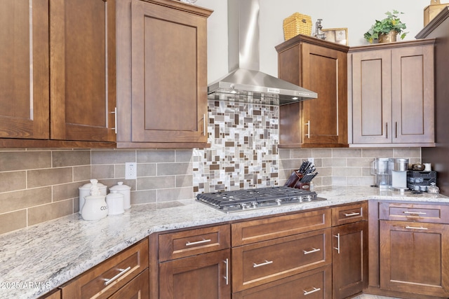 kitchen featuring tasteful backsplash, stainless steel gas cooktop, wall chimney range hood, and light stone counters