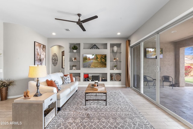 living room with ceiling fan, light wood-type flooring, and built in shelves