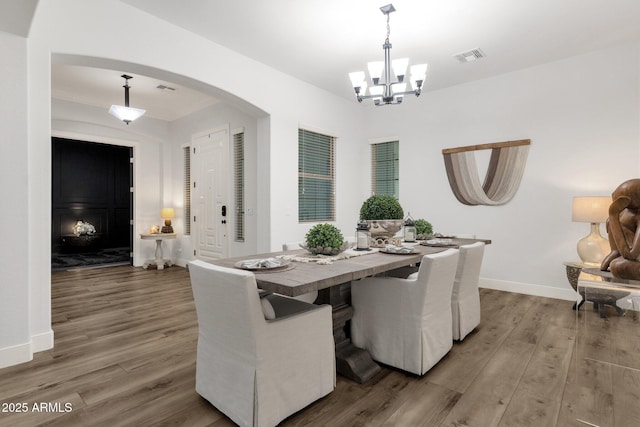 dining space with an inviting chandelier, arched walkways, baseboards, wood finished floors, and visible vents