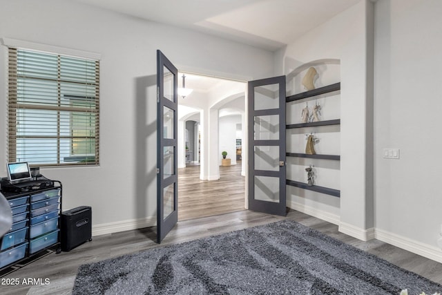 hall featuring arched walkways, french doors, and wood finished floors