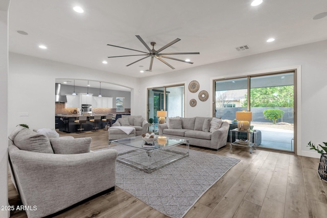 living room with arched walkways, light wood-style flooring, a ceiling fan, recessed lighting, and visible vents
