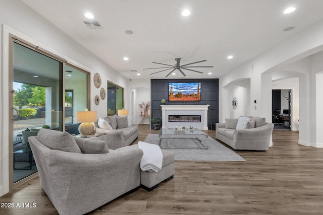 living room featuring visible vents, arched walkways, a glass covered fireplace, and a ceiling fan