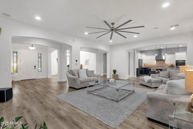 living room with arched walkways, a ceiling fan, light wood finished floors, and visible vents