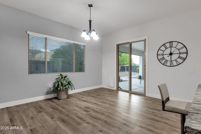 unfurnished dining area featuring baseboards, wood finished floors, and a notable chandelier