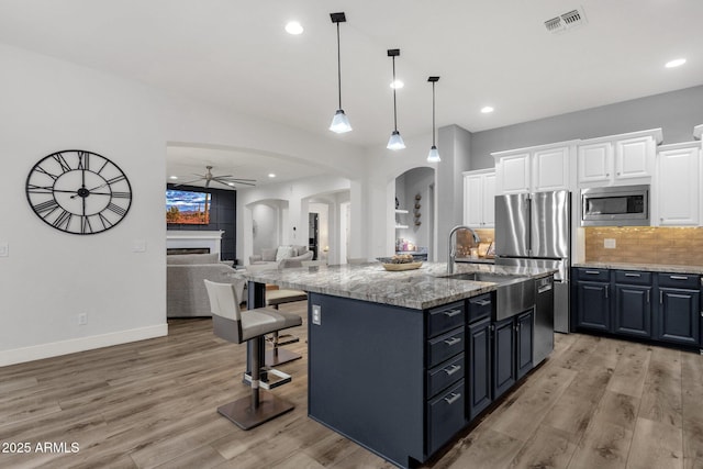 kitchen with ceiling fan, visible vents, appliances with stainless steel finishes, arched walkways, and light wood-style flooring