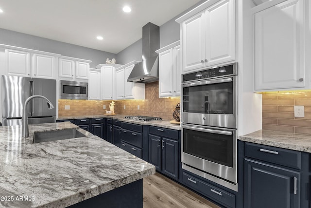 kitchen featuring wall chimney range hood, recessed lighting, white cabinetry, tasteful backsplash, and appliances with stainless steel finishes