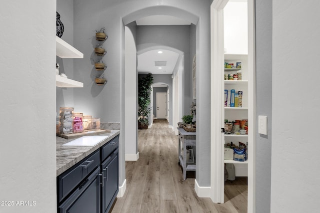 corridor featuring light wood-style floors, arched walkways, baseboards, and visible vents
